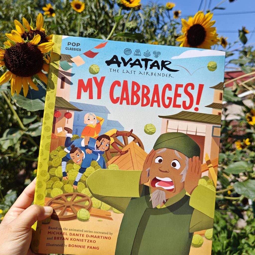 hand holding up copy of My Cabbages in front of sunflowers