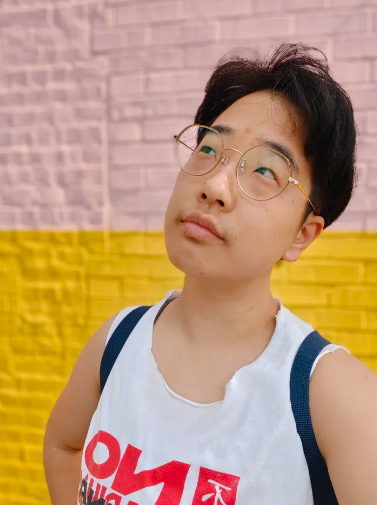 Jessica standing in front of a pink and yellow brick wall wearing a No Arena in Chinatown t-shirt